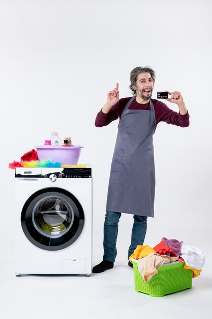 Front view happy man holding card standing near washing machine on white background