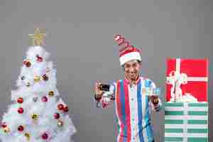 Free photo front view happy man holding card and travel ticket around xmas tree