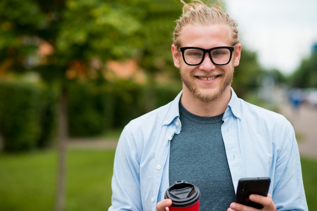 スマートフォンとカップを屋外で幸せな男の正面図