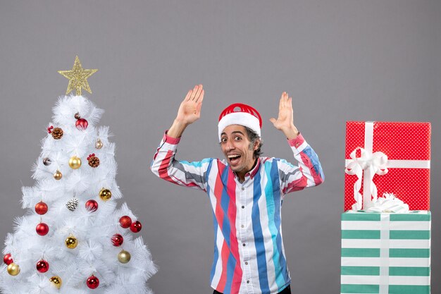 Front view happy man putting his hands up near white xmas tree