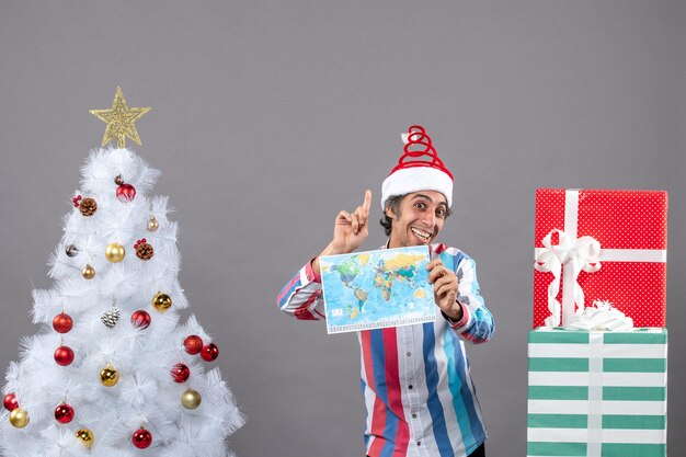 Front view happy man with spiral spring santa hat looking at high holding world map pointing at high