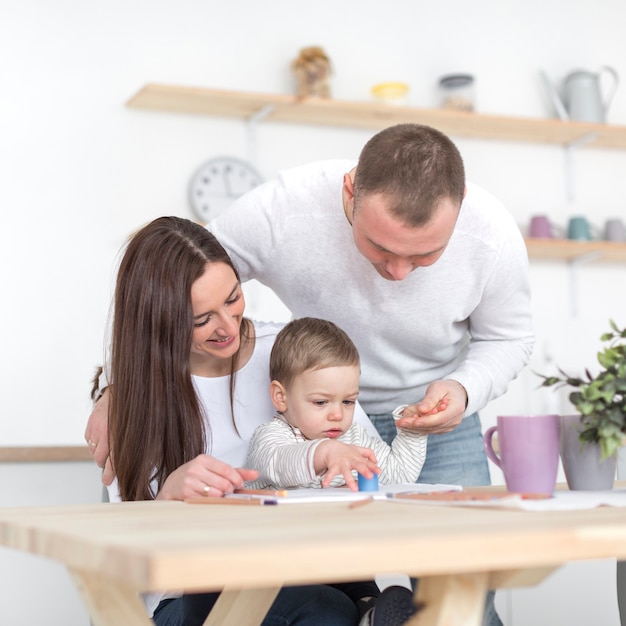 Front view of happy parents with baby in the kitchen