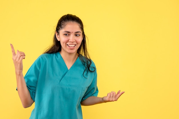 黄色の背景に手を開いて幸せなきれいな女性医師の正面図