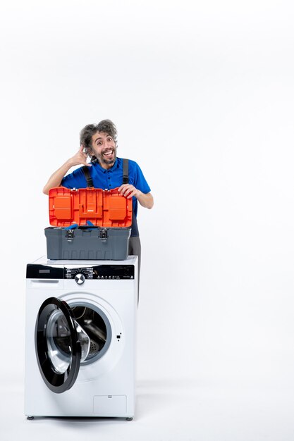 Front view happy repairman making call me gesture behind washing machine on white space