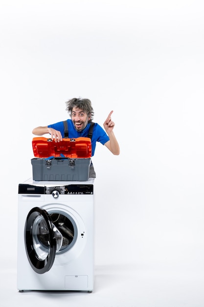 Front view happy repairman opening tools bag behind white washing machine on white space