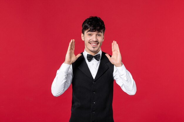 Front view of happy satisfied male waiter in a uniform with butterfly on neck on red background