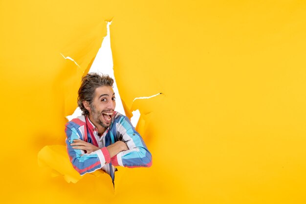 Front view of a happy smiling and ambitious young guy posing for camera through a torn hole in yellow paper