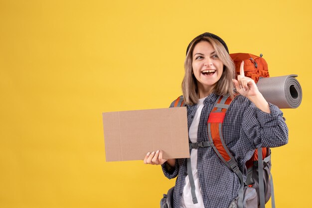 Front view of happy traveler woman with backpack holding cardboard