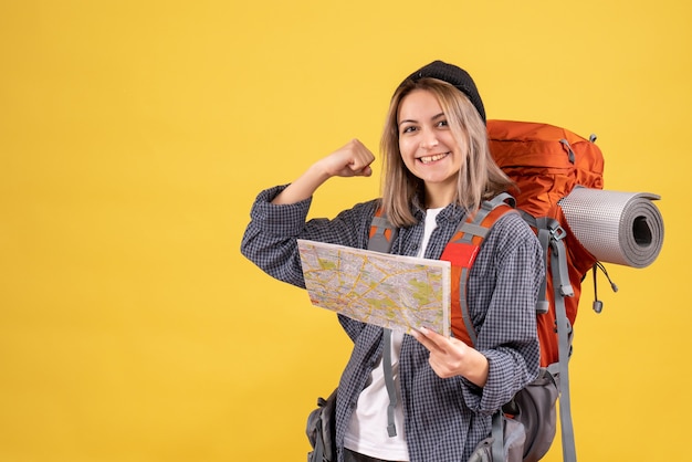 Front view of happy traveler woman with backpack holding map showing arm muscle