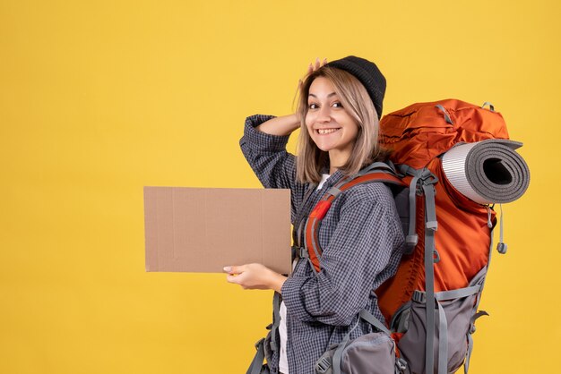 Front view of happy traveler woman with red backpack holding cardboard