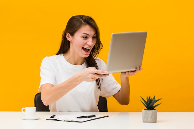 Front view happy woman at desk holding up laptop