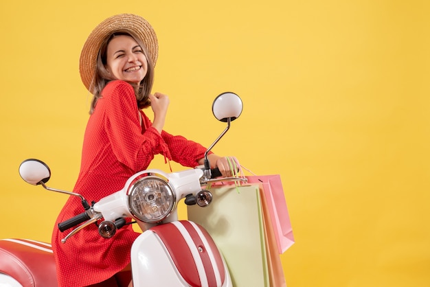 Front view of happy woman in red dress on moped holding shopping bags