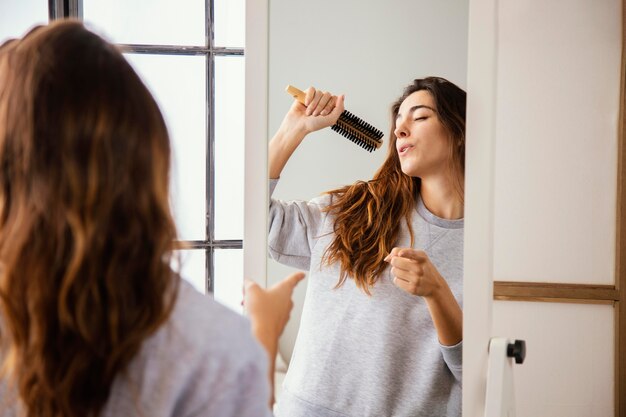 Front view of happy woman singing into hairbrush at home