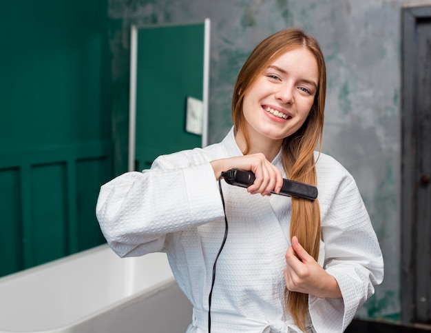 Front view of happy woman straightening her hair