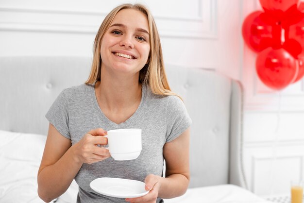 Front view happy woman with coffee in bedroom