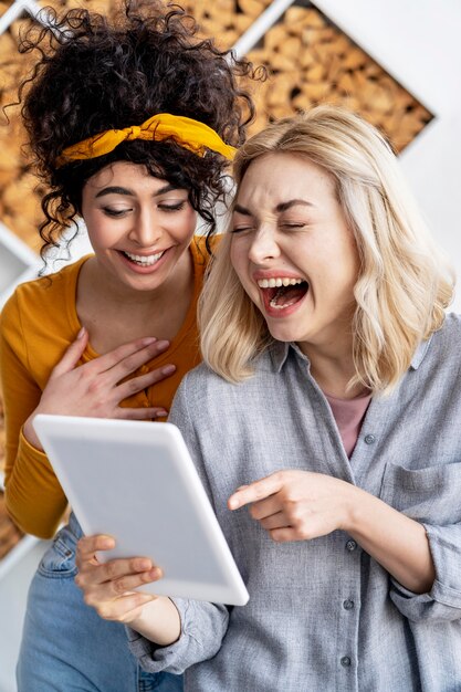 Front view of happy women laughing and holding tablet