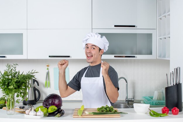 Front view happy young cook in uniform standing in kitchen