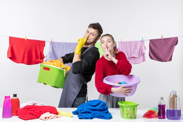 Front view of happy young couple making hush sign holding washing stuffs on white wall