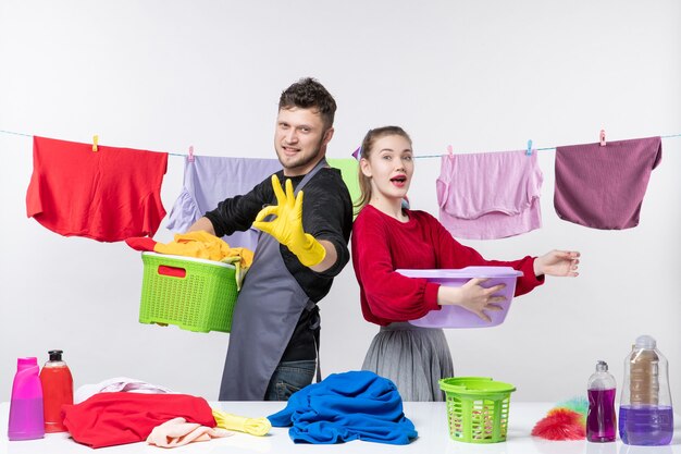 Front view of happy young couple man making okey sign wife holding washtub on white wall