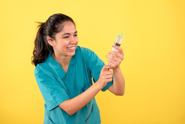 Front view happy young female doctor with syringe on yellow background