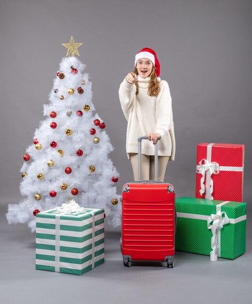 クリスマスツリーの近くに立っている赤いスーツケースを持つ正面図幸せな少女
