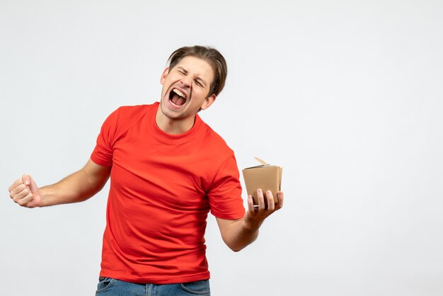 Front view of happy young guy in red blouse holding small box on white background