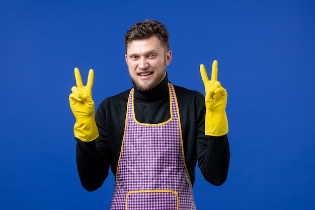 Front view of happy young male making victory sign standing on blue wall