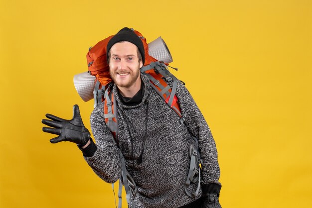 Вид спереди счастливого молодого человека с кожаными перчатками и рюкзаком, махнув рукой