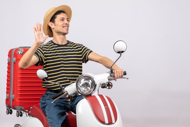 Front view of happy young man with straw hat on moped waving hand