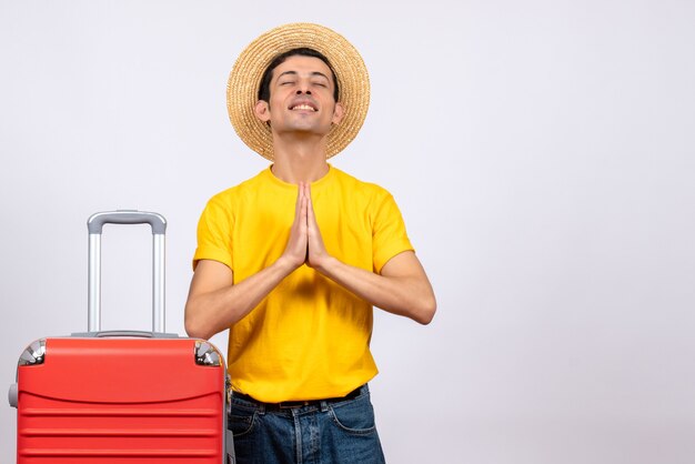 Front view happy young man with yellow t-shirt and suitcase joining hands together