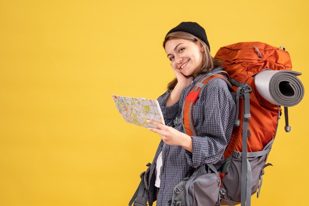 Front view of happy young traveller with backpack holding map standing on yellow wall