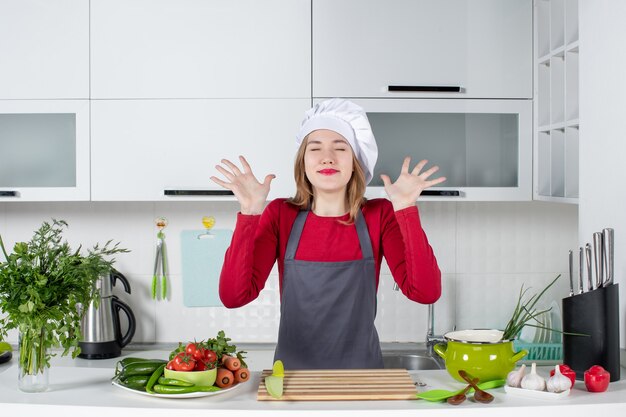 Front view happy young woman in apron with closed eyes raising hands