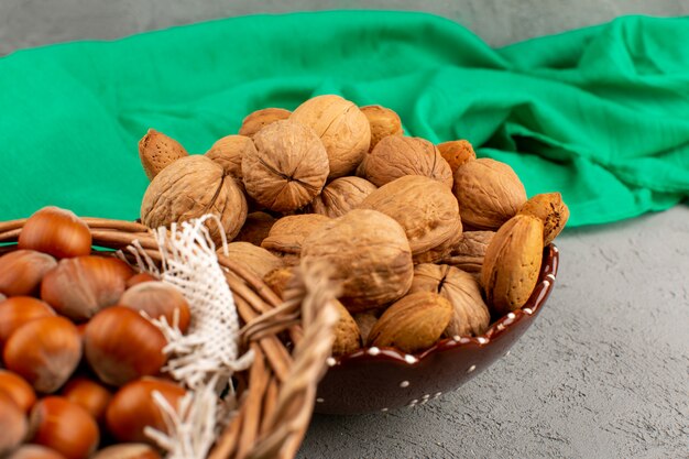 front view hazelnuts and walnuts whole inside plate and basket on the dark desk