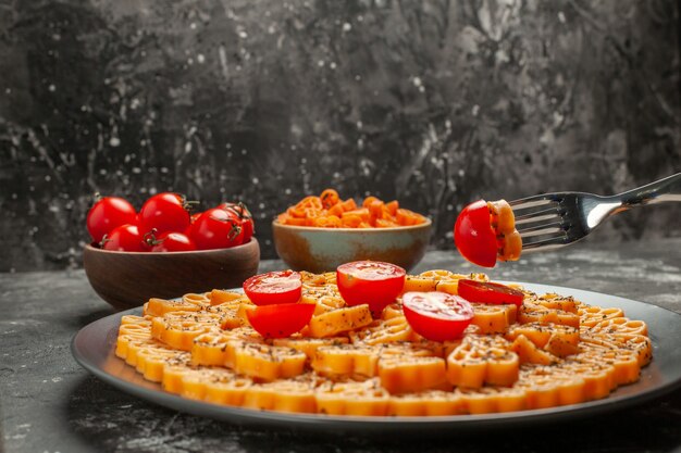 Front view heart italian pasta with tomatoes on round plate tomatoes in bowl on dark backgrund