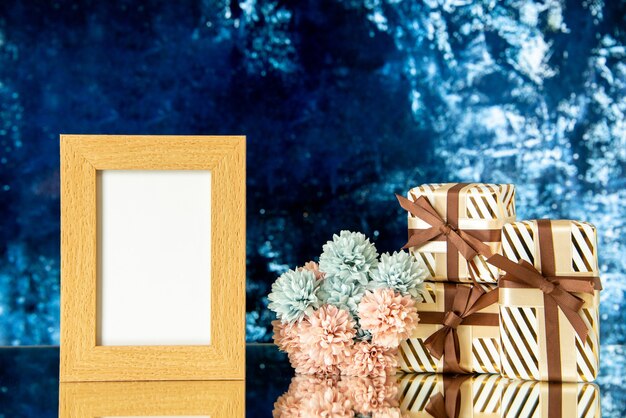 Front view holiday gifts empty picture frame flowers reflected on mirror on dark blue background