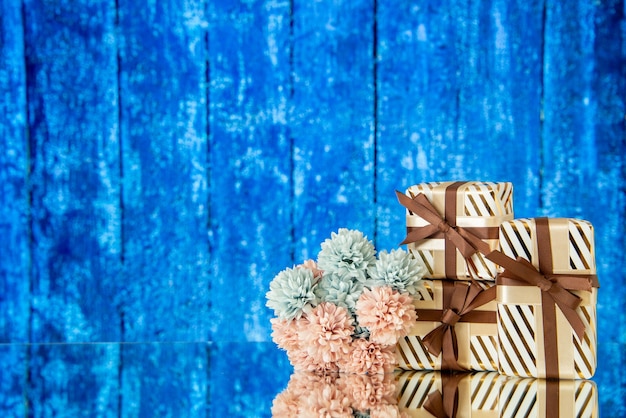 Front view holiday gifts flowers reflected on mirror on blue wooden background