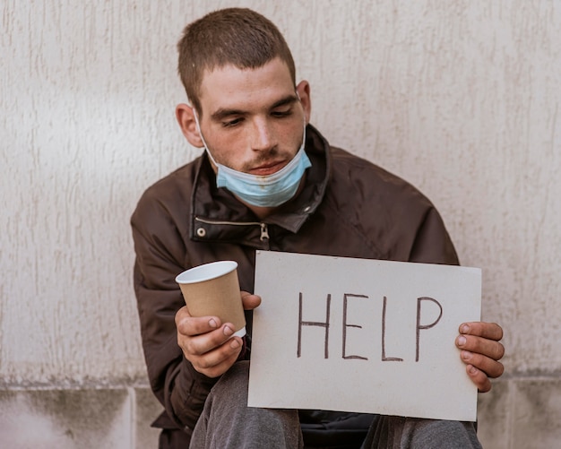 Front view of homeless man holding cup and help sign