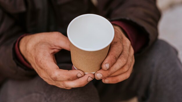 空のカップを保持しているホームレスの男性の正面図