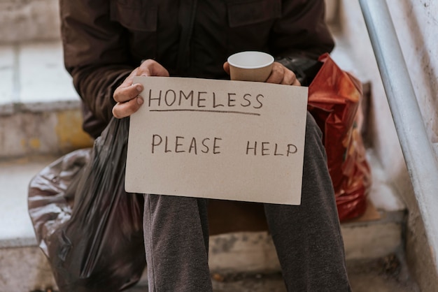 Front view of homeless man holding help sign and plastic bag