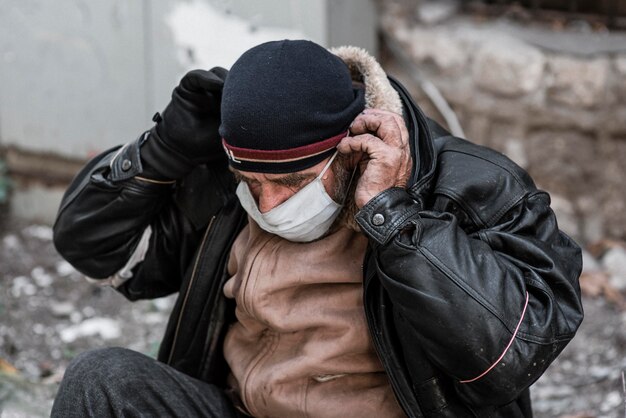 Front view of homeless man outdoors putting on medical mask