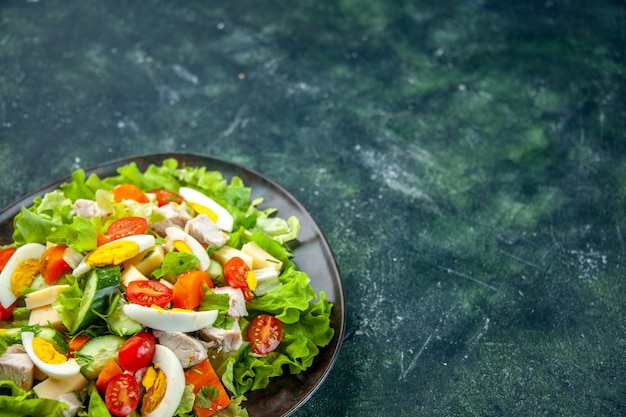 Front view of homemade delicious salad with many ingredients in a plate on the right side on black green mix colors background with free space