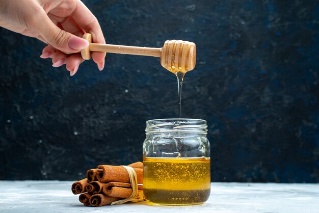 A front view honey and cinnamon female dunking spoon into the honey on the blue-grey background sugar  plant