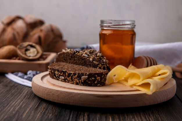 Вид спереди мед в банке с черным хлебом и сыром на подставке с грецкими орехами на деревянном фоне