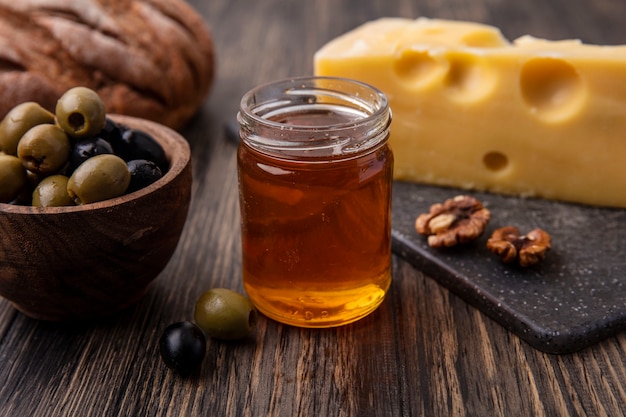 Вид спереди мед в банке с сыром маасдам на подставке и оливками на столе