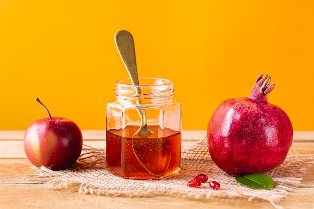 Front view honey jar with spoon and fruits