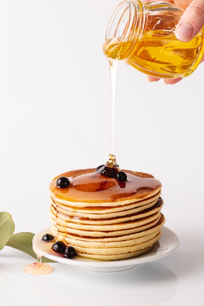 Front view honey poured over pancake tower on plate with blueberries