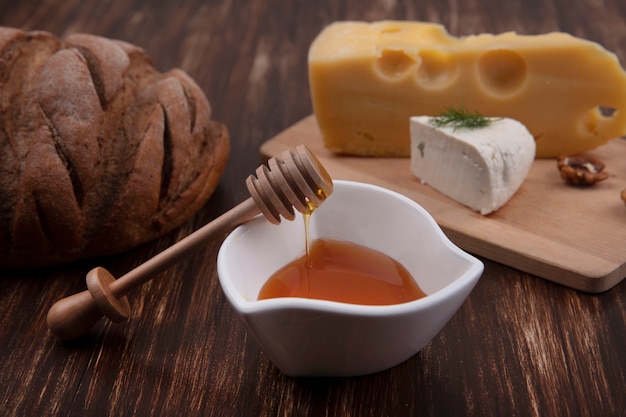 호두와 나무 배경에 빵 한 덩어리와 함께 스탠드에 다양한 치즈와 함께 접시에 전면보기 꿀