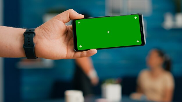 Front view of horizontal isolated mock up green screen chroma key display of modern phone. Two collegues talking about internet browsing and social media in home studio background