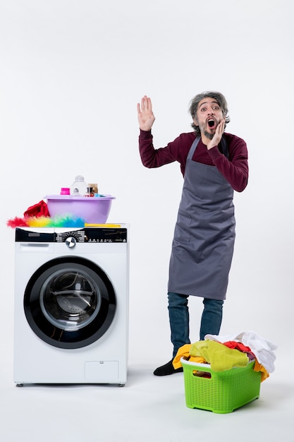 Front view housekeeper man calling someone standing near washer laundry basket on white background