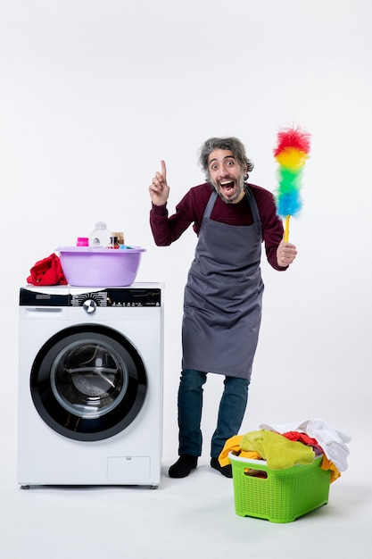 Free photo front view housekeeper man holding duster standing near washing machine laundry basket on white background